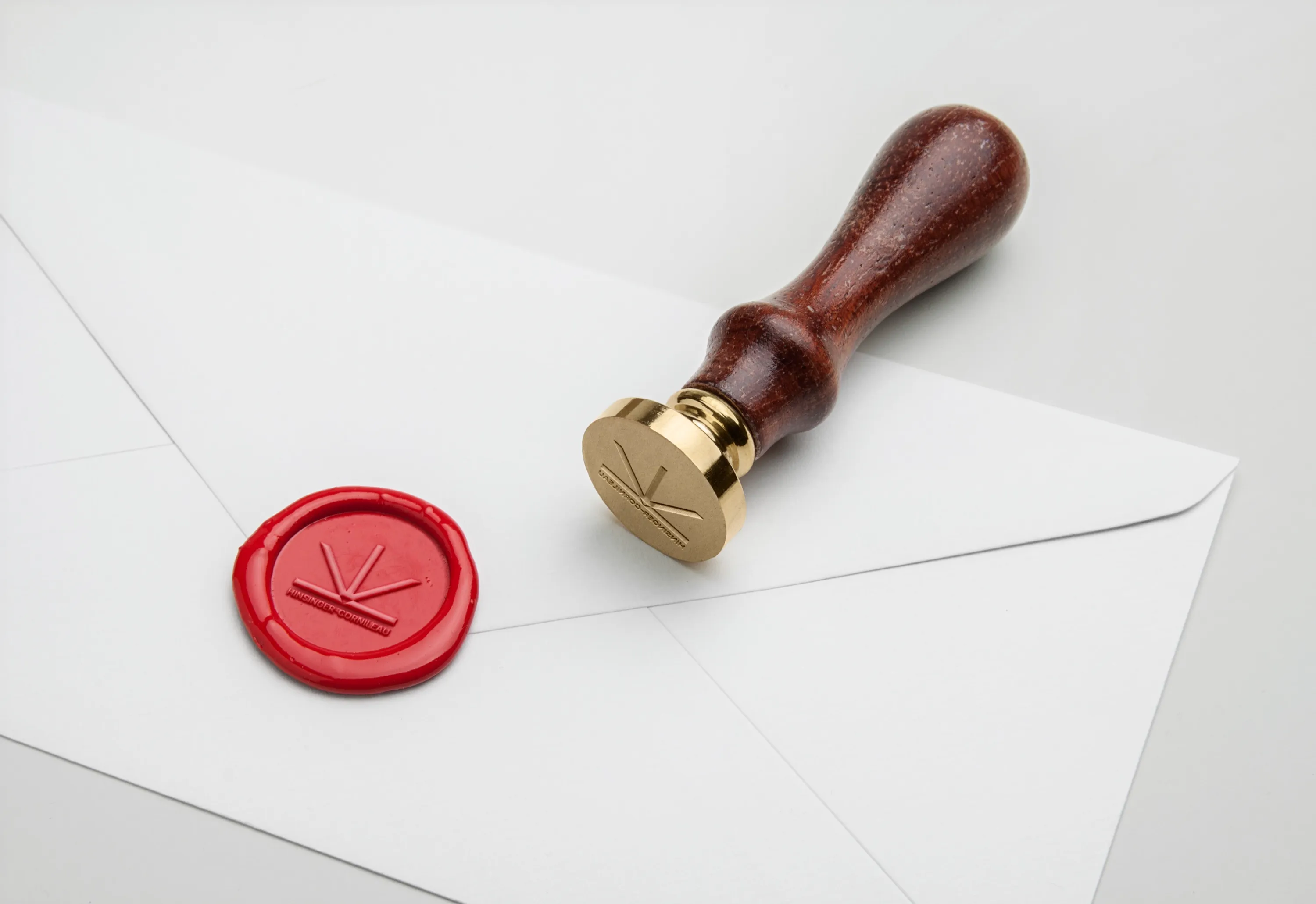 Un cachet de cire rouge frappé du logo Hinsinger-Cornileau sur une enveloppe blanche, à côté du tampon en laiton